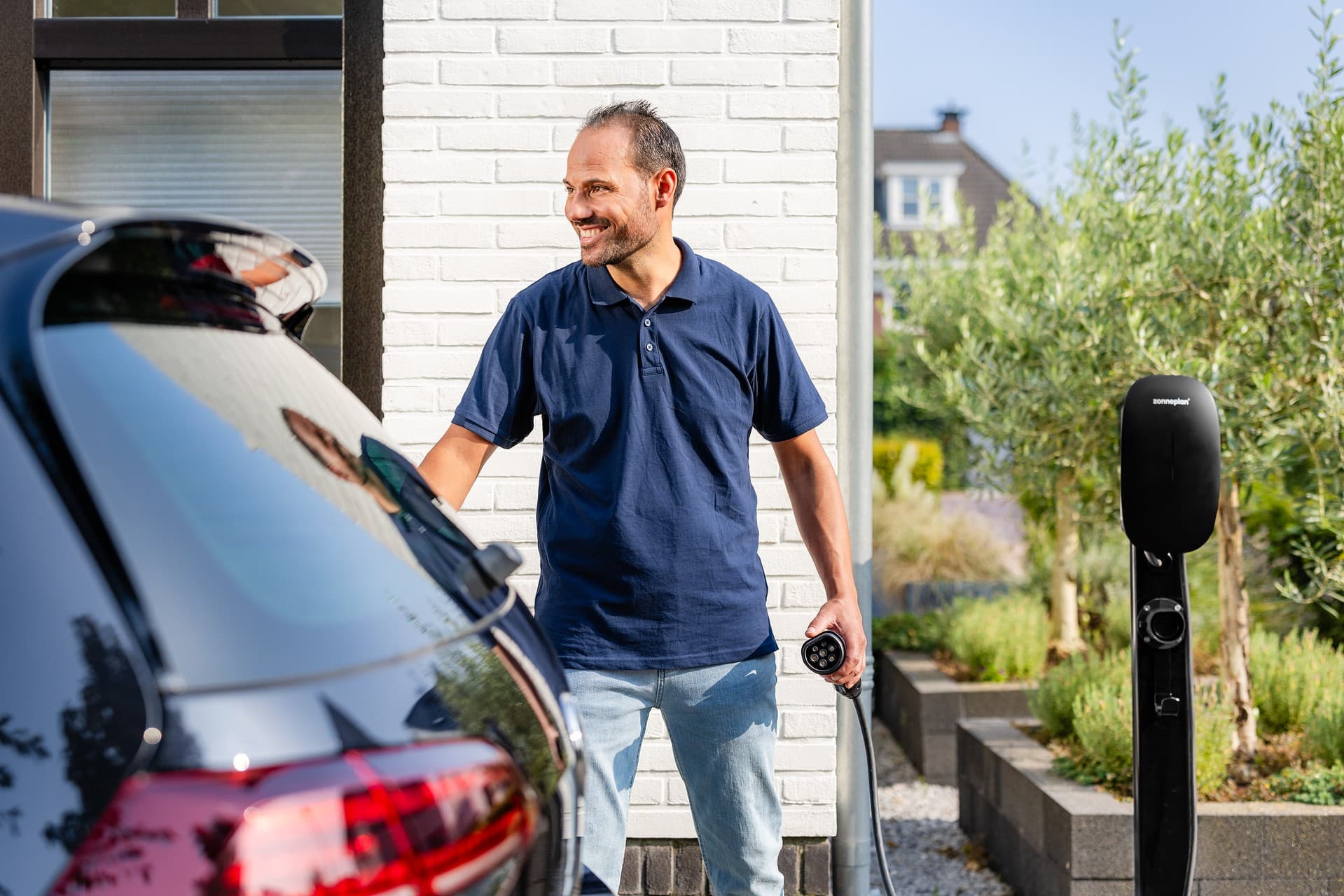 Man bij auto met elektrische laadpaal en laadstekker in zijn hand